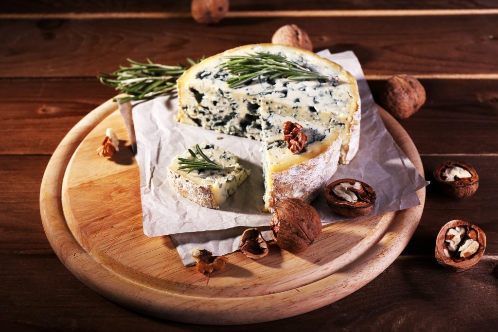 Blue cheese with sprigs of rosemary and nuts on board with sheet of paper and wooden table background