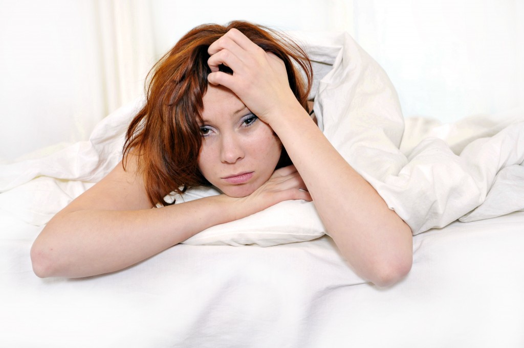 red hair woman on bed waking up with hangover and headache