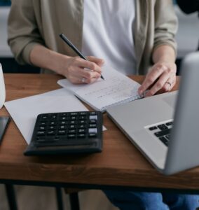 Kobieta licząca na kalkulatorze przy laptopie i notesie