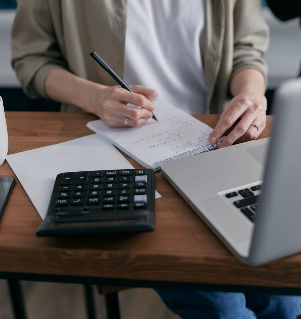 Kobieta licząca na kalkulatorze przy laptopie i notesie